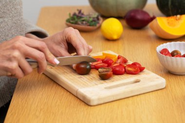 Dişi eller, kiraz domateslerini tahta kesme tahtasıyla sebze dilimliyor. Vejetaryen yemekleri kavramı