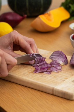 Ahşap kesme tahtasının üzerinde taze malzemelerle kırmızı soğan doğrayan kadın elleri. Vejetaryen yemekleri kavramı
