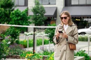  Şehirde çiçeklerle ve yeşilliklerle süslenmiş cep telefonu kullanan güzel bir kadın. İş kadını konsepti, seyahat