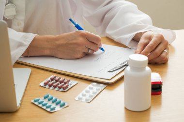 Kadın doktor ilaç ve dizüstü bilgisayarla reçete yazıyor. Pratisyen hekim klinikte bir tıbbi kayıt formu dolduruyor. Tıbbi hizmet