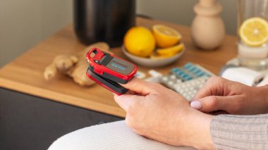 Beyaz kadın evde sağlık kontrolü için parmak üzerinde kırmızı titreşim oksimetresi kullanıyor. Sağlık hizmetleri