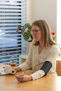 Beyaz bir kadın kan basıncını evde ölçüyor. Sağlık hizmeti kavramı