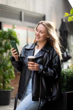 Şehir ortamında kahve ve akıllı telefondan hoşlanan beyaz bir kadın. Güzel kadın.