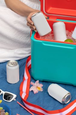 Elinde içecek kutusu olan bir kadın termos kutusunun üzerinde buz küpleriyle birlikte yakın çekim yapıyor. Pikniğe geri dönüşümlü teneke kutuda soğuk içecek alan bir kadın. Boş ambalaj