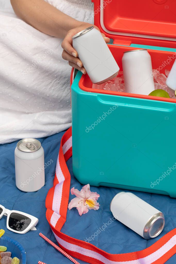 Woman holding beverage can with copy space over thermos box with ice cubes closeup. Lady taking cold drink in mockup recyclable tin on picnic. Blank packaging