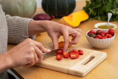 Dişi eller, kiraz domateslerini tahta kesme tahtasıyla sebze dilimliyor. Vejetaryen yemekleri kavramı