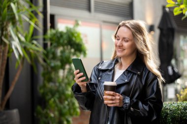 Şehir ortamında kahve ve akıllı telefondan hoşlanan beyaz bir kadın. Güzel kadın.