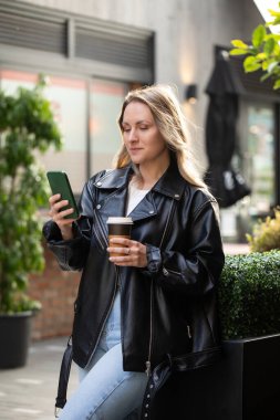 Şehir ortamında kahve ve akıllı telefondan hoşlanan beyaz bir kadın. Güzel kadın.