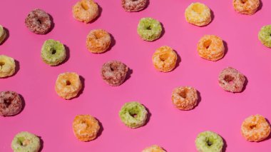 Kahvaltı ve yemek tasarımı için pembe arka planda renkli mısır gevreği halkaları. Kahvaltı kavramı