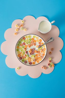 Pembe paspasın üzerinde renkli mısır gevreği ve mavi arka planda süt. Kahvaltı kavramı