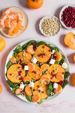 Taze hurma ve turunçgil salatası, ıspanak, feta ve pembe masada nar. Kış salatası. Noel salatası konsepti. 