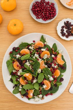 Mandalinalı taze ıspanak salatası, ahşap masada nar ve peynir. Vejetaryenler için bayram ve Noel salatası.