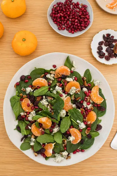 Mandalinalı taze ıspanak salatası, ahşap masada nar ve peynir. Vejetaryenler için bayram ve Noel salatası.