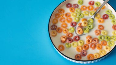 Mavi arka planda sütlü renkli sağlıklı kahvaltı gevreği ve sabah yemekleri için kaşık. Boşluğu kopyala
