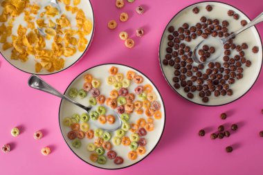 Farklı türde kahvaltı gevreği arka planında pembe arka planda süt var. Çikolata topları, mısır gevrekleri ve renkli yüzükler.