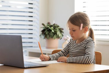 Genç kız parlak odada dizüstü bilgisayar ve defterle öğreniyor. Çevrimiçi okulda okuyan tatlı bir kız. Eğitim kavramı.