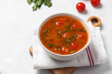 Domatesli taze sebze çorbası ve keten peçetedeki beyaz kasede otlar. Vejetaryen menüsü. 