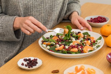  Tahta masada taze ıspanak, mandalina ve nar ile kış salatası yiyen kadın. Vejetaryenler için bayram ve Noel salatası.