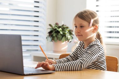 Evde dizüstü bilgisayar ve defterle e-öğrenim yapan mutlu genç bir kız. Eğitim kavramı.