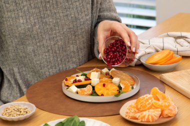 Kış salatasına hurma, ıspanak ve peynir serpiştiren bir kadın. Besleyici bir yemek için hurma ve turunçgilli sağlıklı kış salatası.