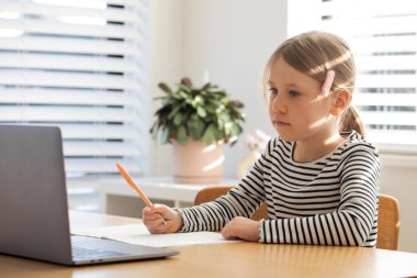 Evde çalışan, dizüstü bilgisayarın başında oturan bir çocuk. Çevrimiçi okulda okuyan tatlı bir kız. Eğitim ve e-öğrenim kavramı.