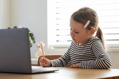 Genç kız parlak odada dizüstü bilgisayar ve defterle öğreniyor. Çevrimiçi okulda okuyan tatlı bir kız. Eğitim kavramı.