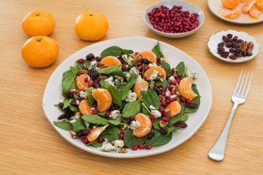Mandalinalı taze ıspanak salatası, ahşap masada nar ve peynir. Vejetaryenler için bayram ve Noel salatası.
