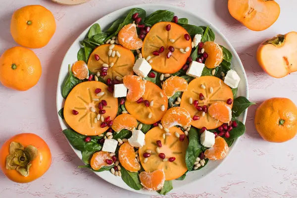 Taze hurma ve turunçgil salatası, ıspanak, feta ve pembe masada nar. Kış salatası. Noel salatası konsepti. 