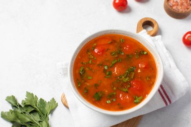Domatesli taze sebze çorbası ve keten peçetedeki beyaz kasede otlar. Vejetaryen menüsü. 