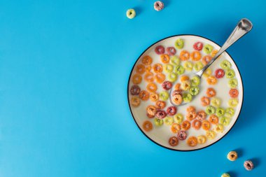 Mavi arka planda sütlü renkli sağlıklı kahvaltı gevreği ve sabah yemekleri için kaşık. Boşluğu kopyala