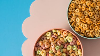  Kahvaltı için yuvarlak mısır gevrekleri ve pastel arka planda renkli halka kaseleri. Farklı türde kahvaltı gevrekleri..