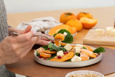 Taze yemek konsepti için turunçgil, hurma ve feta ile sağlıklı kış salatası yiyen bir kadın.