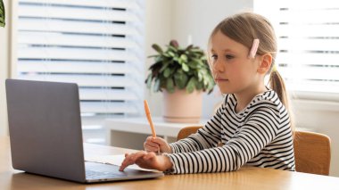 Evde çalışan, dizüstü bilgisayarın başında oturan bir çocuk. Çevrimiçi okulda okuyan tatlı bir kız. Eğitim ve e-öğrenim kavramı.