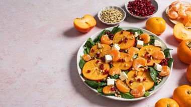 Taze hurma ve turunçgil salatası, ıspanak, feta ve pembe masada nar. Kış salatası. Noel salatası konsepti. Boşluğu kopyala