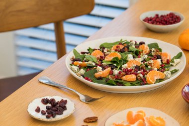 Mandalinalı taze ıspanak salatası, ahşap masada nar ve peynir. Vejetaryenler için bayram ve Noel salatası.
