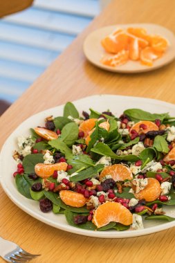 Mandalinalı taze ıspanak salatası, ahşap masada nar ve peynir. Vejetaryenler için bayram ve Noel salatası.