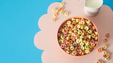 Pembe hasırın üzerinde çok renkli kahvaltılık mısır gevreği ve mavi arka planda süt. Kahvaltı kavramı. Boşluğu kopyala