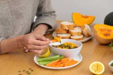 Tahta bir masada dilimlenmiş ekmekle balkabağı humusuna havuç daldıran bir kadın. Sağlıklı gıda kavramı
