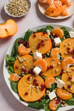 Taze hurma ve turunçgil salatası, ıspanak, feta ve pembe masada nar. Kış salatası. Noel salatası konsepti. 