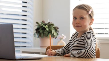 Evde dizüstü bilgisayar ve defterle e-öğrenim yapan mutlu genç bir kız. Eğitim kavramı.