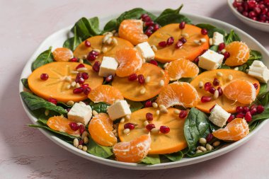 Taze hurma ve turunçgil salatası, ıspanak, feta ve pembe masada nar. Kış salatası. Noel salatası konsepti. 