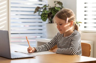 Evde çalışan, dizüstü bilgisayarın başında oturan bir çocuk. Çevrimiçi okulda okuyan tatlı bir kız. Eğitim ve e-öğrenim kavramı.