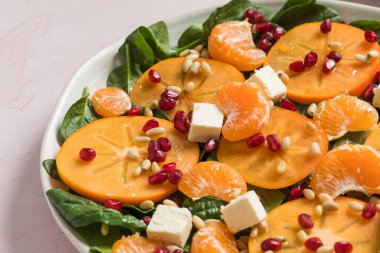 Taze hurma ve turunçgil salatası, ıspanak, feta ve pembe masada nar. Kış salatası. Noel salatası konsepti. 