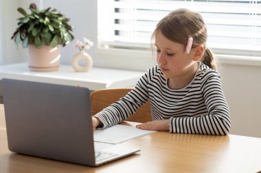 Genç kız parlak odada dizüstü bilgisayar ve defterle öğreniyor. Çevrimiçi okulda okuyan tatlı bir kız. Eğitim kavramı.