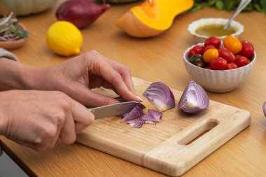 Ahşap kesme tahtasının üzerinde taze malzemelerle kırmızı soğan doğrayan kadın elleri. Vejetaryen yemekleri kavramı