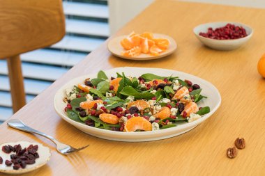 Mandalinalı taze ıspanak salatası, ahşap masada nar ve peynir. Vejetaryenler için bayram ve Noel salatası.