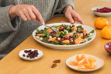  Tahta masada taze ıspanak, mandalina ve nar ile kış salatası yiyen kadın. Vejetaryenler için bayram ve Noel salatası.