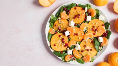 Taze hurma ve turunçgil salatası, ıspanak, feta ve pembe masada nar. Kış salatası. Noel salatası konsepti. Boşluğu kopyala