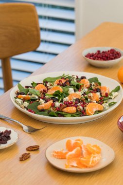 Mandalinalı taze ıspanak salatası, ahşap masada nar ve peynir. Vejetaryenler için bayram ve Noel salatası.
