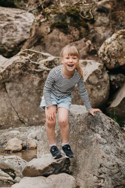 Neşeli tatlı bir kız Yeni Zelanda 'da yürüyüş yaparken kayalara tırmanıyor, doğayı keşfediyor. Çocuklarla seyahat etme kavramı